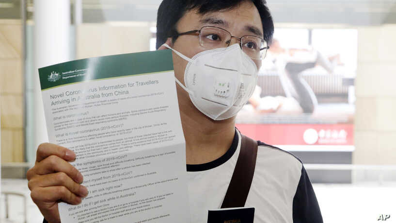 Passenger Kevin Ouyan shows an information pamphlet he was given on arrival at Sydney airport in Sydney Thursday, Jan. 23, 2020, on a flight from Wuhan, China. China closed off a city of more than 11 million people as part of a radical effort to prevent the spread of a deadly virus that has sickened more than 500 people and has begun to spread to other cities and countries in the region. (AP Photo/Rick Rycroft)